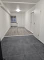 An empty room with tiled flooring, white walls, and a single window. It features a ceiling-mounted light and an open door. There is a radiator beneath the window and two power outlets on the wall.