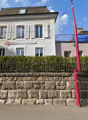 3 story white stucco house, brown roof, white shutters, brick wall, hedges