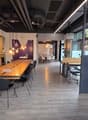 large open space with wood flooring, long wooden table, modern chairs, brick wall, bright windows, office setting