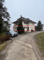 Two story house, white exterior, red roof, multiple windows, car parked in front, trees, grass