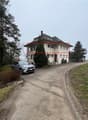 3-story house, beige color, many windows, chimney, paved driveway, a car parked in front