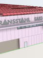 Large industrial or commercial building with a red tiled roof, the name 'Transstahl' prominently displayed on the facade, and a parking area visible in front of the building.