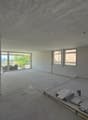 Empty room with white walls, concrete floor, large windows, construction materials on the floor