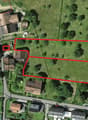 This image shows an aerial view of a residential area with several buildings and a large open green space. The highlighted area appears to be an undeveloped plot of land, possibly a vacant lot or agricultural field. There are some parking spaces visible n