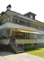 2 story house, beige exterior, brown roof, balcony, stairs, garden, lawn, chimney, multiple windows