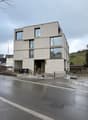 modern design multi-level building, grey concrete walls, glass windows, several trash bins, fenced area, street sign