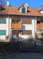 3 story apartment building, brown roof, white walls, wooden balconies, small garden, wooden fence