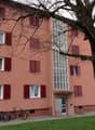 A pink building with multiple windows and red shutters, a tree in front, and bicycles parked outside.
