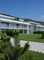 Modern two-story apartment building, white exterior, glass balconies, landscaped front yard