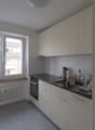 modern white kitchen with gray floor, large window with view, under cabinet sink and dishwasher, built-in oven and dishwasher