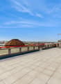 Large open rooftop terrace with tiled flooring, glass railings, and views of the surrounding cityscape. The terrace features a domed structure and other architectural elements.