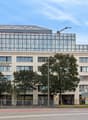Modern office building with glass facade, multiple floors, entrance with glass doors, street with cars and bicycles