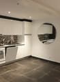 modern kitchen with white cabinets, black tiled backsplash, round mirror, dishwasher, oven, sink, tiled floor
