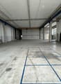 large room with high ceiling, blue lines on the floor, concrete walls, some equipment and furniture