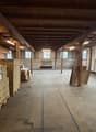 Empty warehouse with wooden beams, fluorescent lights, wooden pallets, stacks of boxes, concrete floor, windows