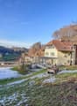 Detached house with red roof, glass windows, snow on the ground, trees, mountains, clear blue sky