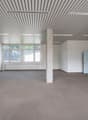 Large open office space with high ceilings, exposed beams, and large windows. The room has a concrete column in the center and a refrigerator in the corner. The space appears to be unfinished and ready for customization.