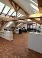 wooden beams, wooden floor, white walls, office desks, monitors, lamps, potted plants