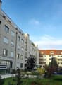 4 story building, balcony, garden with plants and grass, orange house in the background