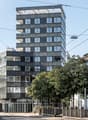 Apartment building with balconies, modern design, multiple windows, grey exterior, sign reading 'Baren Tour'.