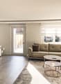 modern living room with white walls, gray floor, two couches, coffee table, TV, white entertainment center, glass door