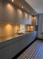 modern kitchen with stainless steel countertops, tiled backsplash, under-cabinet lighting, double sink, gas stove, and a window with a view