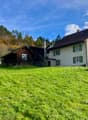 2 story house, brown roof, green shutters, wooden barn, large grassy field, trees in the background