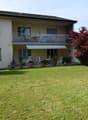 2-story house, beige exterior, terrace on the second floor, lawn, trees, plants, awning over the terrace