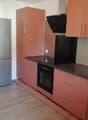 modern kitchen, with oven, refrigerator, brown wooden cabinets, white walls, wooden floor