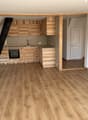 An empty kitchen area with wooden floor, wooden kitchen cabinets, integrated oven and extractor, gas stove, and white radiators on both sides