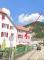 A street view of a building with red shutters and a green fence, with a mountain in the background.