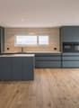 modern kitchen with island, wooden floor, gray cabinets, white countertops, built-in oven, sink, and faucet