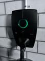 Black electric vehicle charging station with a green LED ring light, mounted on a concrete wall