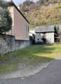 2 buildings, grassy area, stone wall, hill in background
