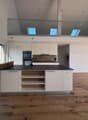 Open kitchen with central island and modern appliances, large windows, wooden floor, balcony, and a high ceiling