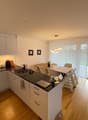 modern kitchen with white cabinets, black countertops, island with sink, dining table, chairs, wooden floor, sliding glass door to patio, pendant light, mirror, framed pictures