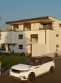 white modern house, large balcony on the first floor, 4 floors, parking, small garden, 2 people standing in front
