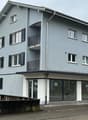three-story apartment building with balconies, modern architecture, gray exterior, glass windows, front entrance