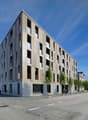 Modern apartment building with multiple floors, concrete and glass exterior, multiple windows, and a flat roof.