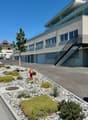Modern apartment building with garage entrance, stairs, parking area, fire hydrant, plants, and curbs.
