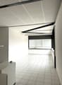 Empty office room with white tiles, modern ceiling with lighting, white walls, window with blinds, and white cabinet in the corner
