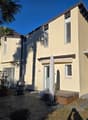 2 story house, yellow exterior, brown roof, balcony, patio, palm trees, barrel, potted plant