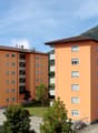Two orange apartment buildings with multiple windows and balconies, surrounded by trees and a parking lot.