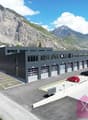 Large commercial building with multiple garage doors, parking lot, surrounded by mountains and vineyards