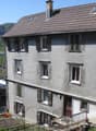 3 story house, brick exterior, 4 windows on each floor, brown roof, chimney, fenced pathway