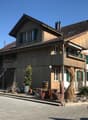 two-story chalet, wooden exterior, green shutters, balconies, surrounded by plants and rocks, mountain in the background