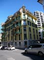 large yellow building with green accents, 4 balconies, multiple cars parked in front