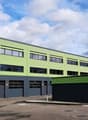 Large green and grey industrial building, several large windows, roll up garage doors on the ground floor, three garages on the side