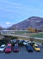 Parking lot with multiple cars parked, mountains in the background, and a building on the right side