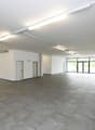 Wide open space, concrete floor, two doors, fire extinguisher, glass walls, white walls, ceiling lights